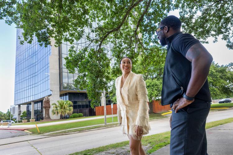 Two people talk on a tree-shaded sidewalk beside a glass office tower on Lake Forest Boulevard.