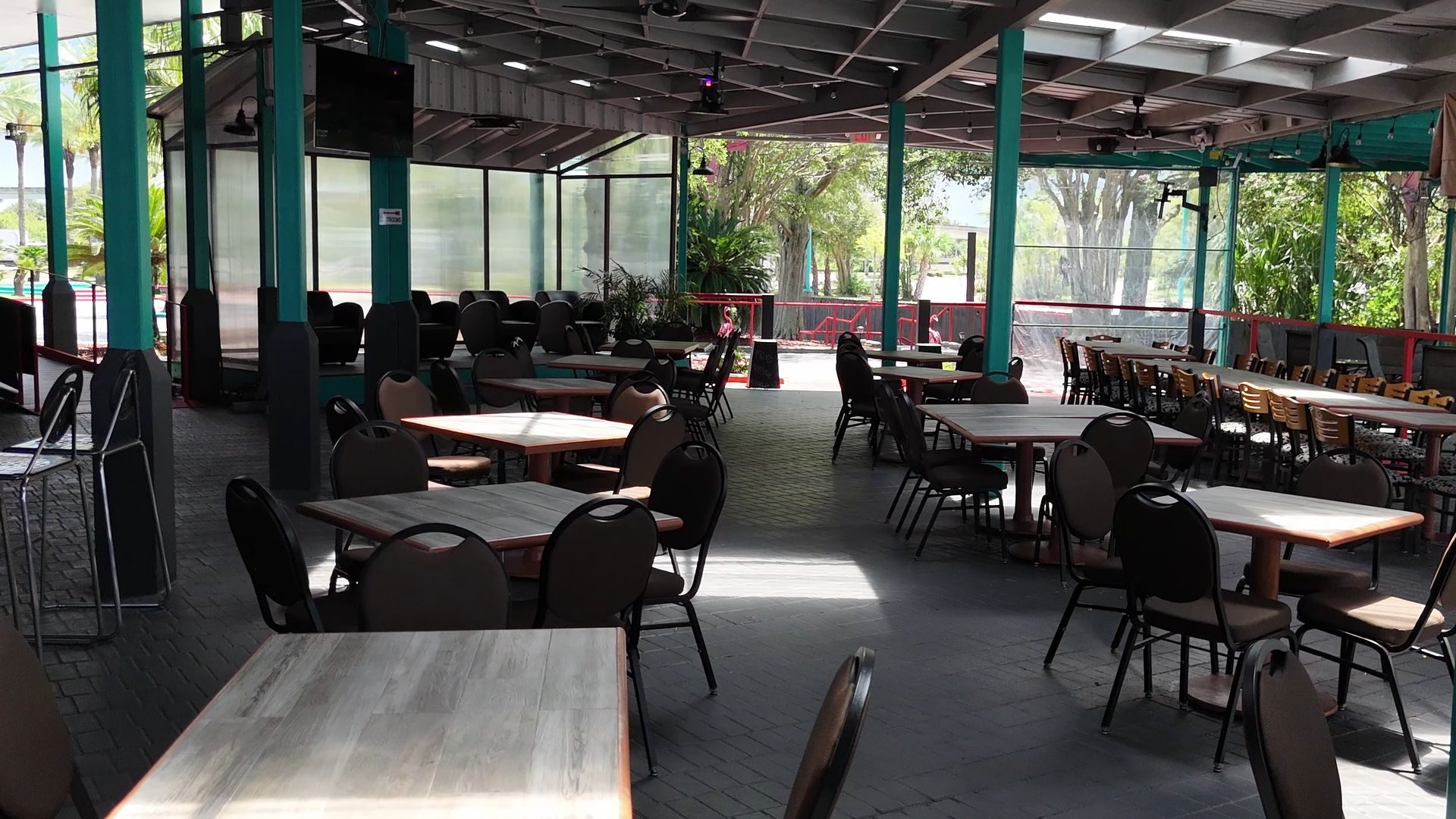 Covered patio dining area with teal columns and wood-top tables, open to the trees.